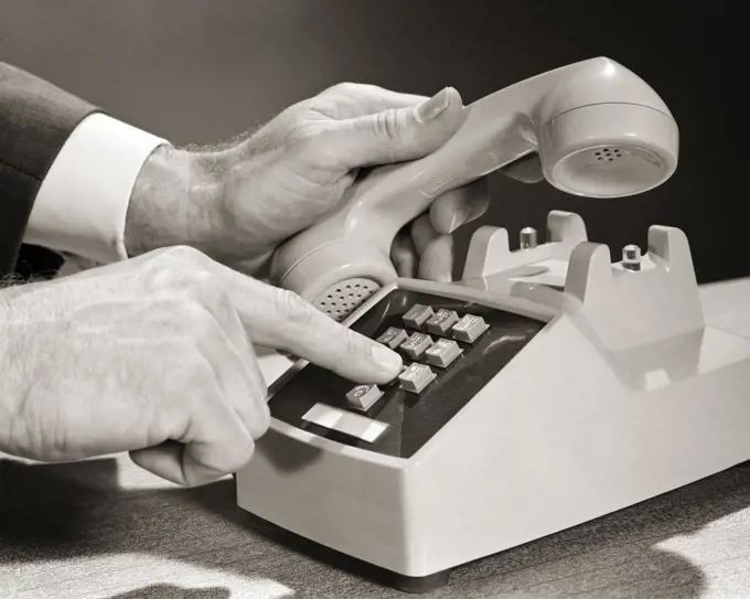 1960s MAN HANDS ONLY LIFTING THE RECEIVER HEAD SET OF TELEPHONE WITH LEFT HAND AND DIALING ON PUSH-BUTTON DIGITS WITH RIGHT HAND