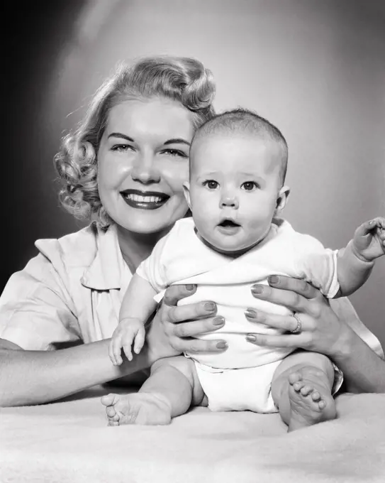 1950s BLONDE MOTHER HOLDING BABY GIRL BOTH LOOKING AT CAMERA
