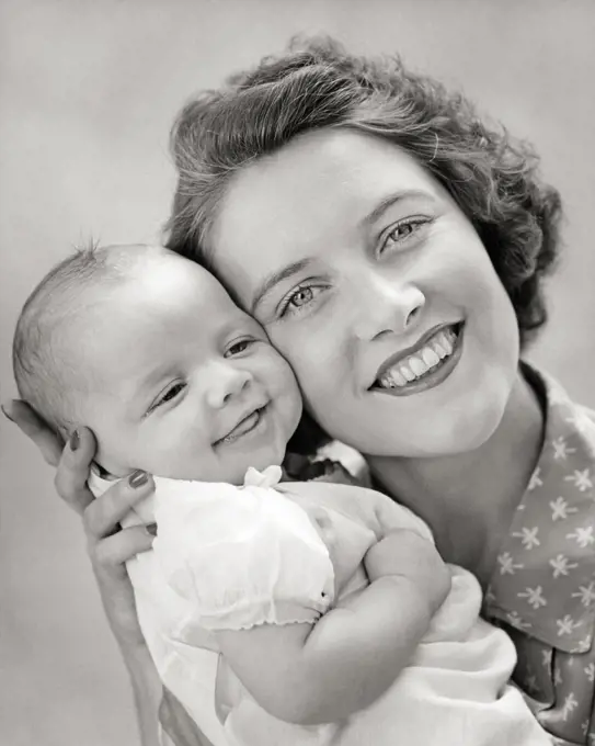 1940s PORTRAIT OF SMILING MOTHER LOOKING AT CAMERA HOLDING BABY DAUGHTER CHEEK TO CHEEK
