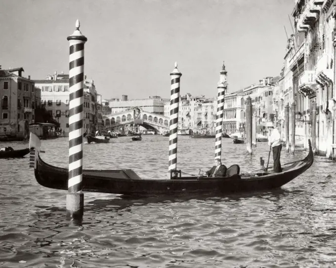 1950s ANONYMOUS BUSINESSMAN RIDING IN GONDOLA ROWING BOAT ON THE GRAND CANAL THE RIALTO BRIDGE IN BACKGROUND VENICE ITALY