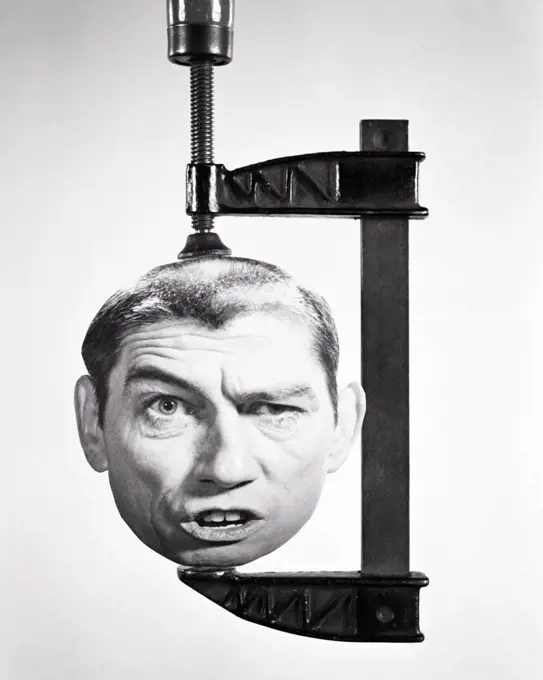 1960S 1970S MANS HEAD WITH FUNNY FACIAL EXPRESSION BEING SQUASHED IN A WOODWORKING CLAMP