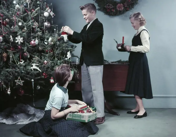 1950S Two Girls And One Boy Decorating Christmas Tree With Ornaments Teens Teenagers Holiday