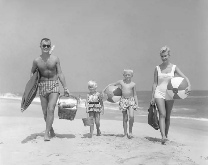 1950S Family Of Four Walking Towards Camera With Beach Balls Umbrella Picnic Basket And Sand Bucket