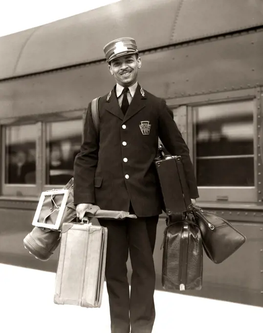 1930S 1940S Portrait Smiling African American Man Red Cap Porter Carrying Luggage Bags Suitcases Passenger Railroad Train