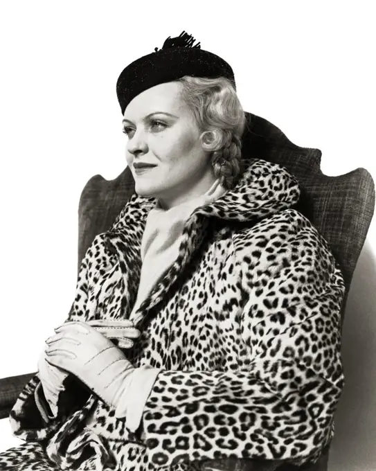 1930s ELEGANT BLONDE WOMAN SITTING IN CHAIR WEARING HAT LEATHER GLOVES AND LEOPARD SKIN COAT