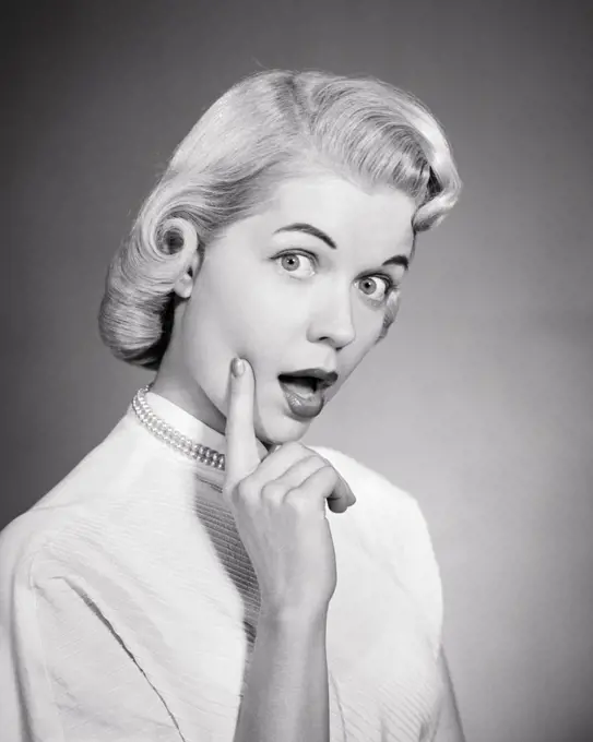 1950s BLONDE WOMAN PAGE BOY HAIR STYLE PEARL NECKLACE WHITE BLOUSE FINGER TOUCHING FACE THOUGHTFUL EXPRESSION LOOKING AT CAMERA