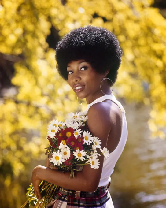1970s SMILING AFRICAN AMERICAN WOMAN WEARING HOOP EARRINGS WHITE TANK TOP HOLDING A BOUQUET SPRING FLOWERS LOOKING AT CAMERA
