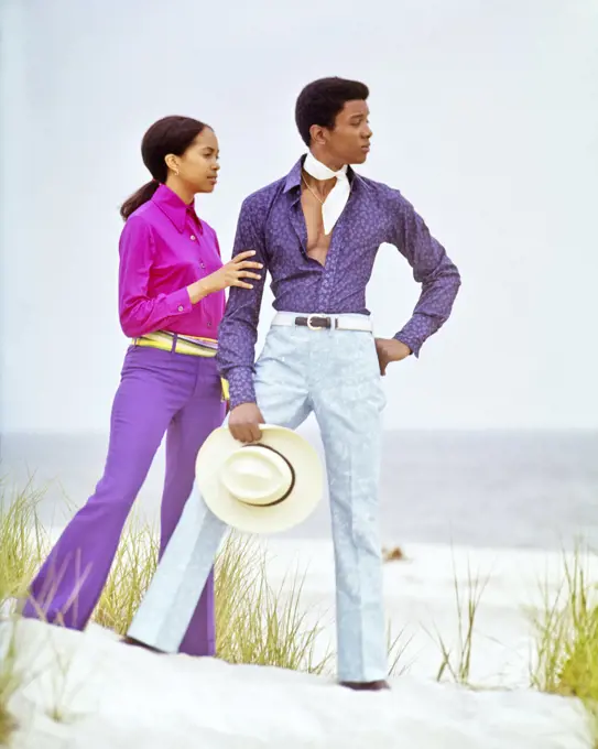 1970s YOUNG ADULT AFRICAN AMERICAN COUPLE STANDING ON BEACH DUNE WEARING COLORFUL SHIRTS BELL BOTTOM PANTS LONG ISLAND NYC USA