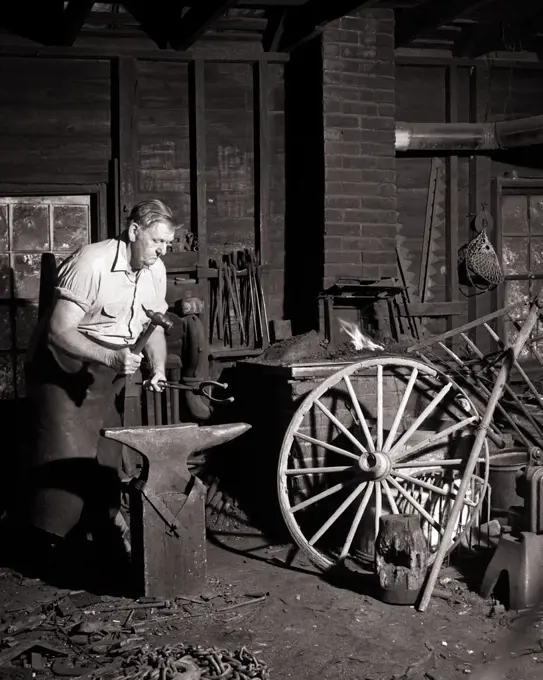 1950s 1960s MAN LOCAL VILLAGE BLACKSMITH WORKING AS FARRIER SHAPING A HORSESHOE WITH HAMMER ON ANVIL IN FORGE VIRGINIA USA