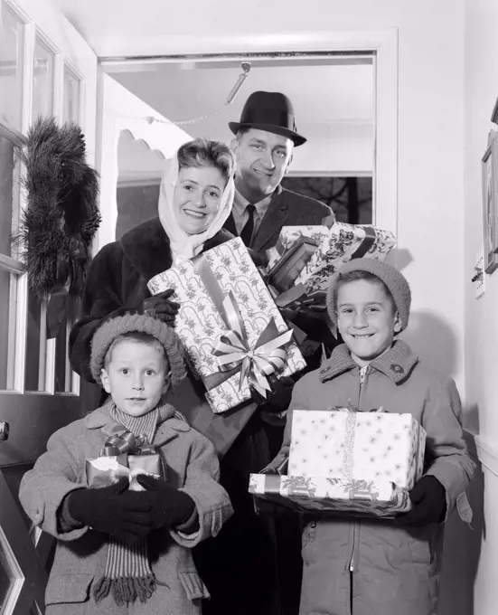1960S Family Standing In Doorway Of Home Wearing Winter Coats & Hats Holding Wrapped Gifts