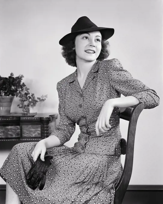 1930s 1940s ATTRACTIVE YOUNG WOMAN PROFESSIONALLY BUSINESS DRESSED IN SUIT WEARING MANNISH HAT SEATED HOLDING PAIR OF GLOVES 