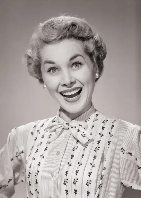 1950s PORTRAIT OF BLOND WOMAN EYES WIDE OPEN BIG SMILE WEARING PRINT STRIPE BLOUSE THAT TIES AT THE NECK LOOKING AT CAMERA
