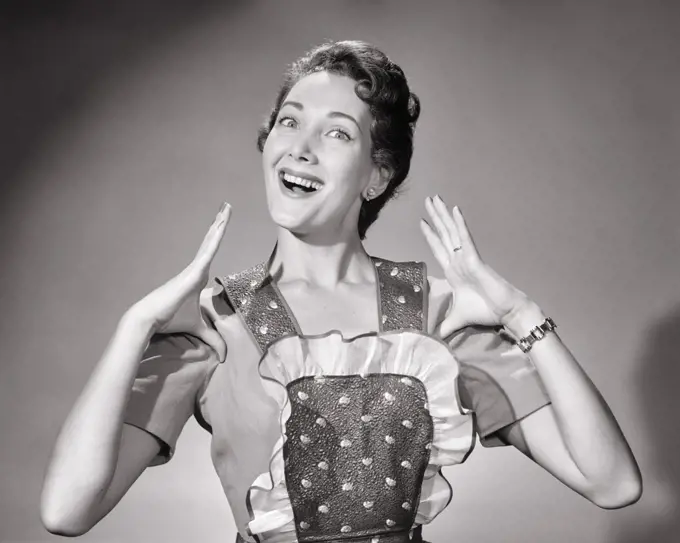1950s PROUD BRUNETTE HOUSEWIFE SMILING WEARING APRON MAKING GESTURE OF THUMBS TUCKED LOOKING AT CAMERA
