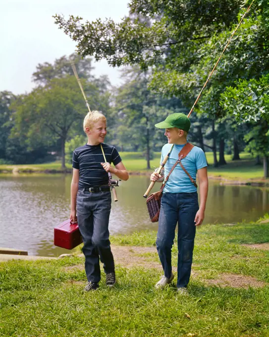 1970s TWO BOYS WALKING ALONG LAKESIDE TALKING CARRYING FISHING POLES AND TACKLE BOXES