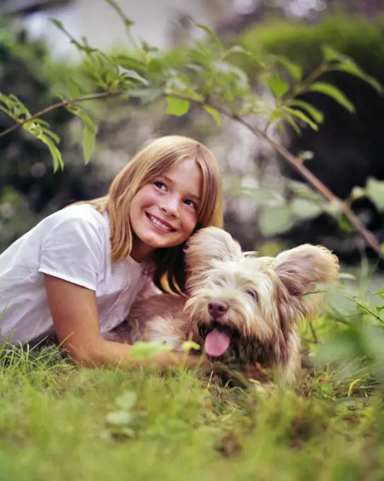1960s SMILING BLOND GIRL LYING IN GRASS PLAYING WITH HER SHAGGY PET DOG