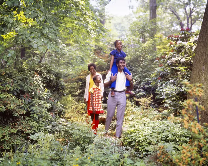 1970s AFRICAN-AMERICAN FAMILY WALKING IN WOODLAND NATURE TRAIL PARK MOTHER FATHER DAUGHTER AND SON RIDING ON DADS SHOULDERS
