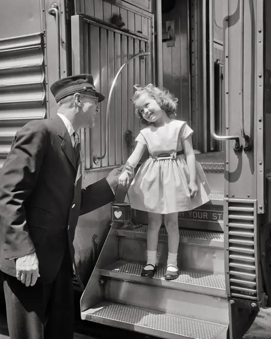 1950s MAN PASSENGER RAILROAD CONDUCTOR IN UNIFORM GREETING SMILING LITTLE GIRL WEARING DRESS AND MARY JANE SHORES ON TRAIN STEPS
