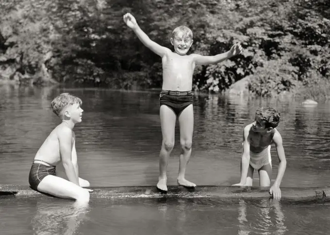 1930s 1940s THREE BOYS FRIENDS BROTHERS PLAYING TOGETHER BALANCING ON FLOATING LOG IN RURAL SWIMMING HOLE WEARING BATHING SUITS
