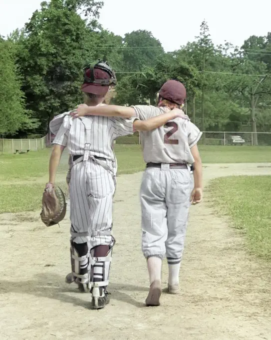 1970s BACK VIEW OF PAIR OF LITTLE LEAGUERS WALKING OFF OF FIELD WITH ARMS AROUND EACH OTHER