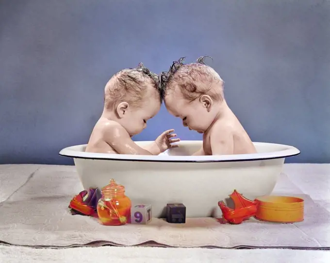 1950s TWIN BABIES SITTING HEAD TO HEAD IN METAL BATH TUB