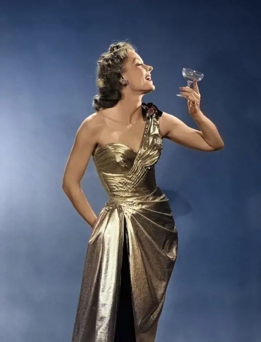 1950s WOMAN WEARING METALLIC EVENING GOWN HOLDING UP WINE GLASS PROFILE