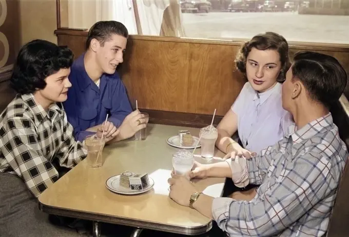1950s TWO TEENAGE COUPLES AT BOOTH IN DINER WEARING PLAID AND SOLID COLOR SHIRTS DRINKING SODAS TALKING TOGETHER