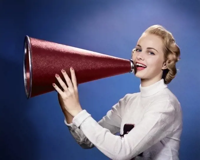 1950s BLONDE WOMAN COLLEGE CHEERLEADER IN LETTER SWEATER LOOKING AT CAMERA YELLING INTO MEGAPHONE
