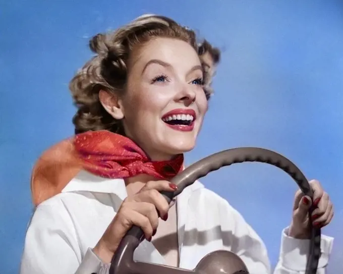 1950s SMILING WOMAN WITH HANDS ON STEERING WHEEL WITH WIND BLOWING BACK HAIR & SCARF STUDIO OUTDOOR