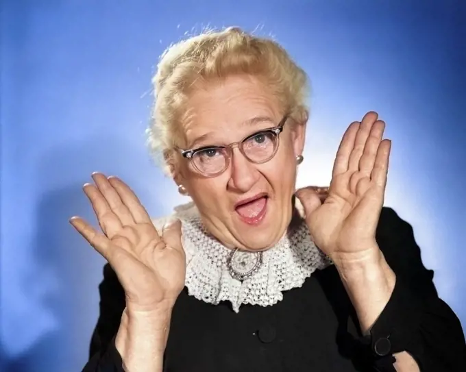 1960s ELDERLY WOMAN IN GRANNY GLASSES HOLDING HAND UP NEAR FACE WITH MOUTH OPEN LOOKING AT CAMERA