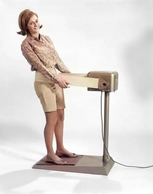 1960s SMILING YOUNG WOMAN STANDING ON WEIGHT REDUCING VIBRATING EXERCISE MACHINE LOOKING AT CAMERA