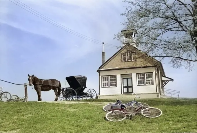 1950s AMISH ONE-ROOM SCHOOLHOUSE AT TOP OF HILL HORSE & BUGGY & BICYCLES PARKED OUTSIDE LANCASTER PA USA