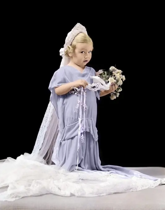 1940s LITTLE BLOND GIRL IN OVERSIZED WEDDING GOWN & VEIL HOLDING BOUQUET WITH CONFUSED EXPRESSION LOOKING AT CAMERA