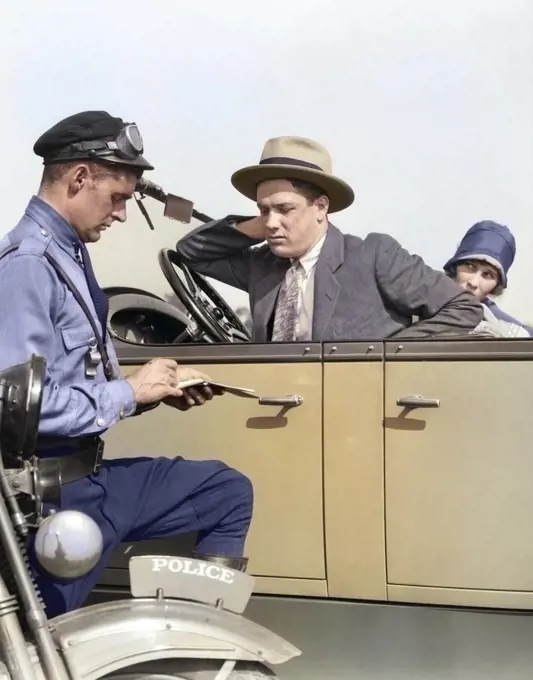 1920s MOTORCYCLE POLICEMAN WRITING A SPEEDING TICKET TO A COUPLE SITTING IN CONVERTIBLE FOUR-DOOR SEDAN AUTOMOBILE