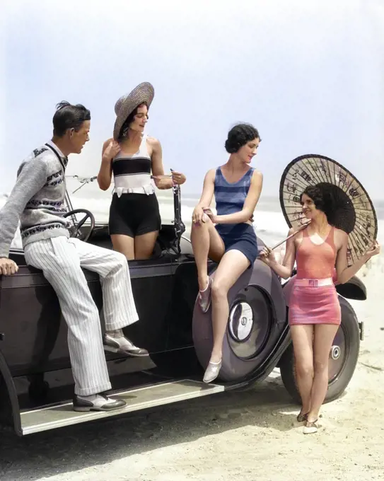 1920s MAN AND THREE WOMEN IN BEACH CLOTHES OR BATHING SUITS POSING AROUND CAR ON RUNNING BOARD AT SEASHORE