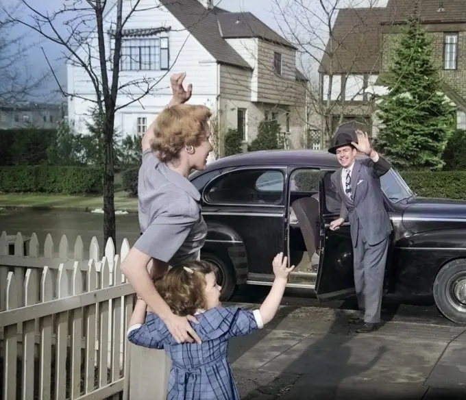 1940s 1950s MOTHER AND DAUGHTER WAVING TO FATHER OPENING AUTOMOBILE DOOR IN FRONT OF SUBURBAN HOME