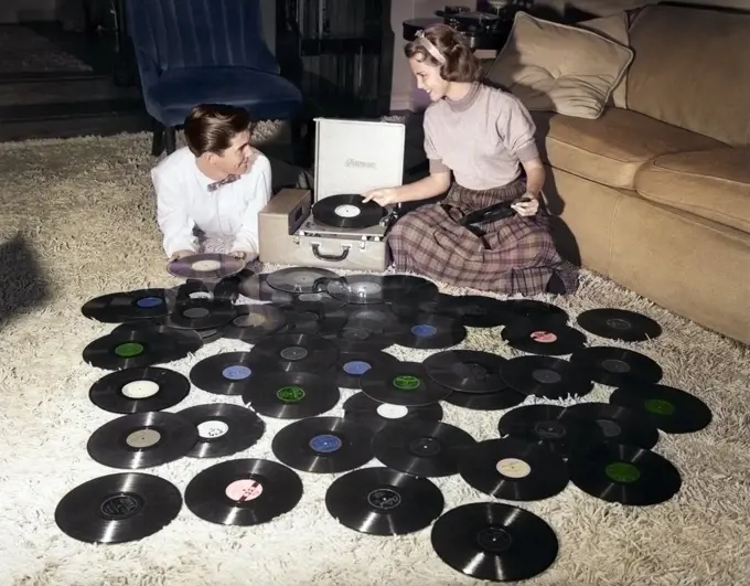 1950s TEENAGE COUPLE PLAYING MANY VINYL MUSIC RECORDS SPREAD OUT ON LIVING ROOM FLOOR