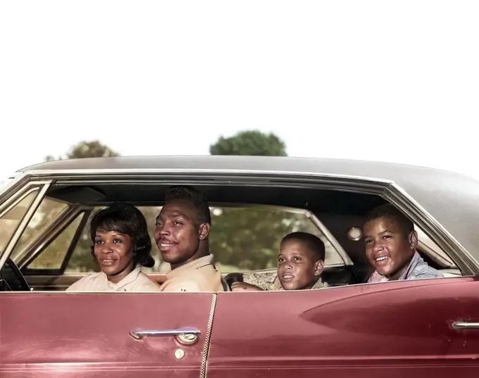1960s SIDE VIEW OUTDOOR SMILING AFRICAN AMERICAN FAMILY FATHER MOTHER TWO SONS RIDING IN FOUR DOOR SEDAN AUTOMOBILE