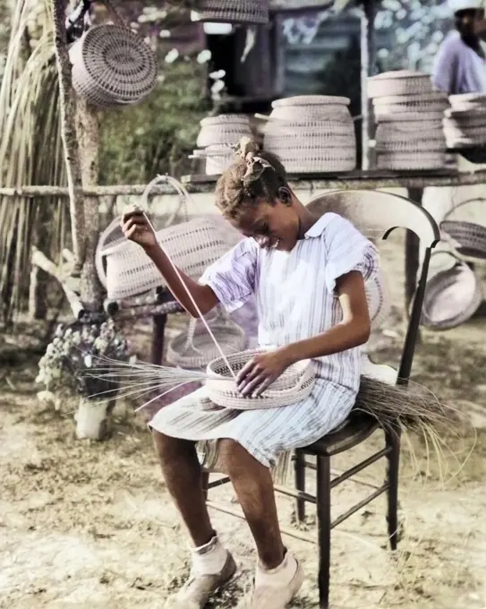 1930s 1940s ANONYMOUS SMILING YOUNG AFRICAN-AMERICAN GULLAH GIRL WEAVING MAKING BASKET FROM SWEETGRASS SOUTH CAROLINA USA