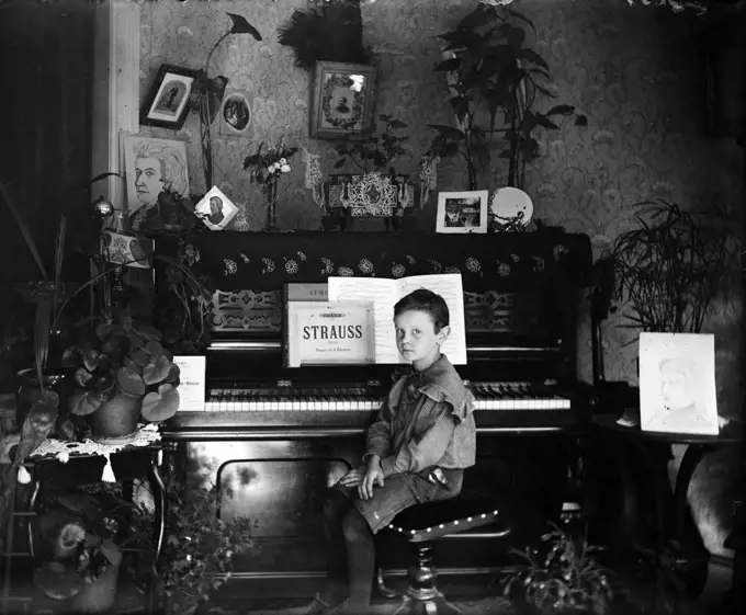 1890s TURN OF CENTURY BOY SITTING AT UPRIGHT PIANO LOOKING AT CAMERA STRAUSS SHEET MUSIC