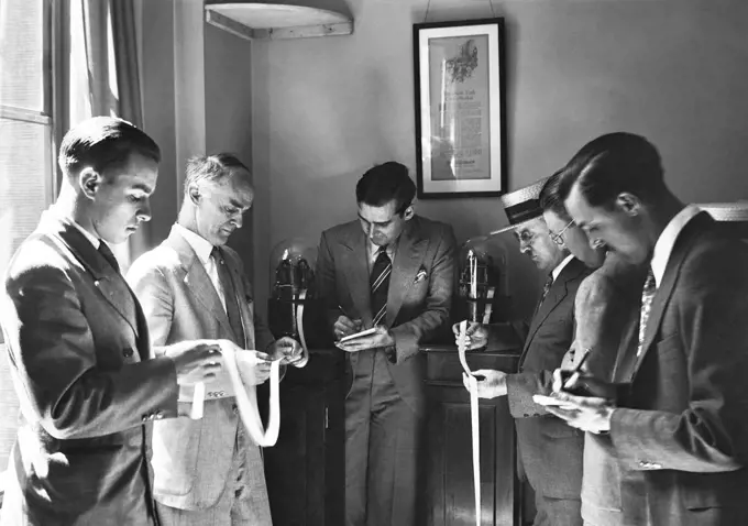 1930s SIX ENGROSSED INVESTORS AND STOCK BROKERS READING PAPER TICKER TAPE INVENTED IN 1867 BY EDWARD CALAHAN NEW YORK CITY USA