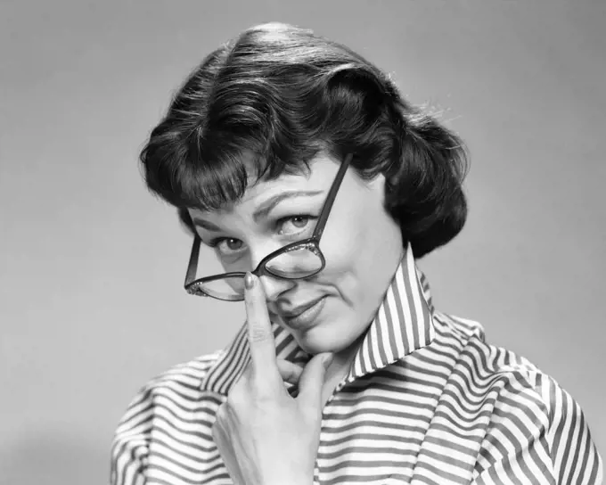 1950s 1960s BRUNETTE WOMAN WEARING EYE GLASSES LOOKING UP WITH DOUBTFUL SKEPTICAL EXPRESSION LOOKING AT CAMERA