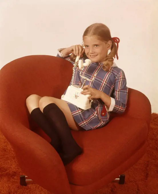 1970s SMILING GIRL KNEE SOCKS PLAID DRESS SITTING RED CHAIR TALKING PHONE TELEPHONE