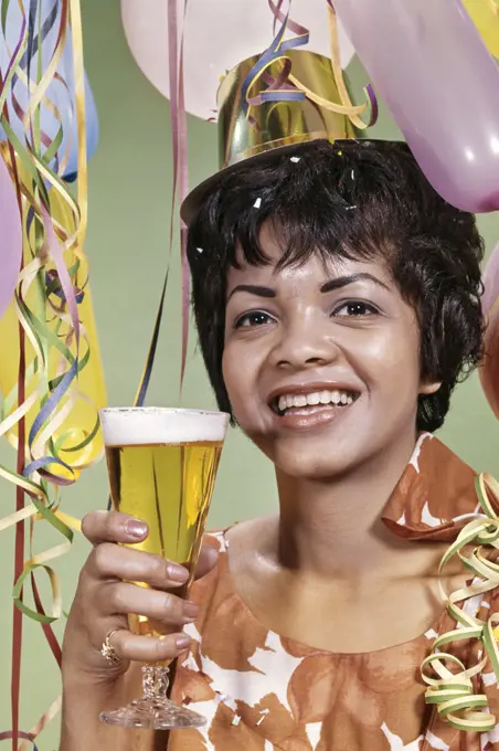 1960s SMILING AFRICAN AMERICAN WOMAN PARTY HAT STREAMERS BALLOONS TOASTING PILSNER GLASS OF BEER 