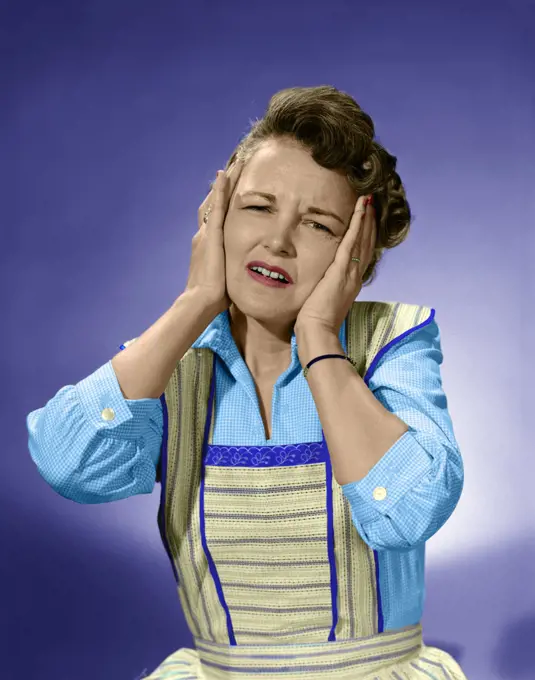 1950s WOMAN IN COTTON DRESS WITH BOTH HANDS OVER HER EARS HOLDING HER HEAD FROWNING LOOKING AT CAMERA