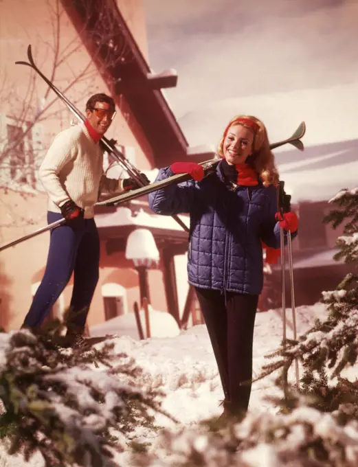1970s COUPLE MAN WOMAN HOLDING SKIS SKI POLES SKI CHALET LODGE SNOW PINE TREES CLOTHES FASHION LIFESTYLE