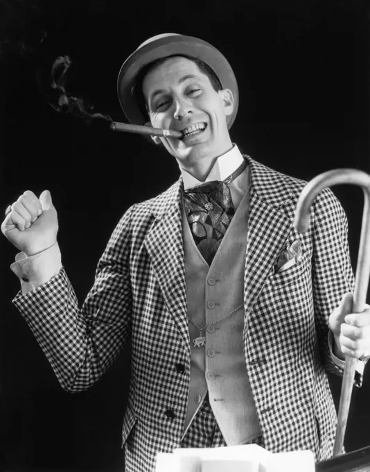 1930s SMILING MAN CARNIVAL BARKER CON MAN IN CHECKERED SUIT WITH CANE IN HAND & CIGAR IN MOUTH LOOKING AT CAMERA