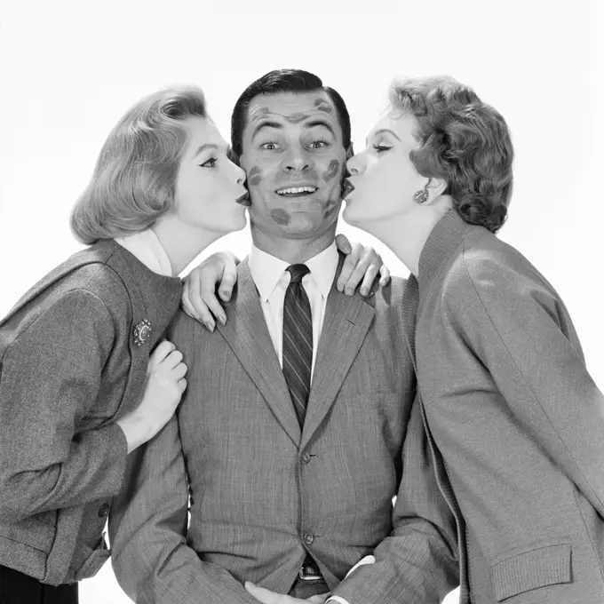 1950s 1960s SMILING SINGLE MAN LOOKING AT CAMERA BEING KISSED BY TWO WOMEN