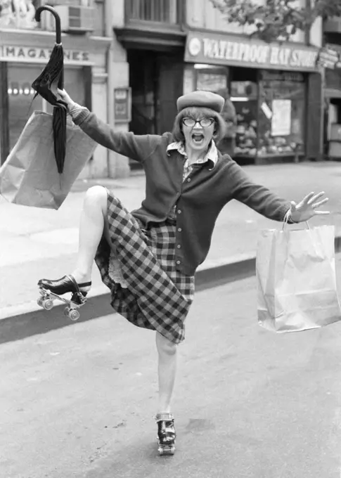 1970s CRAZY WILDLY GESTURING SHOPPING BAG LADY WOMAN ON ROLLER SKATES ON CITY STREET LOOKING AT CAMERA 