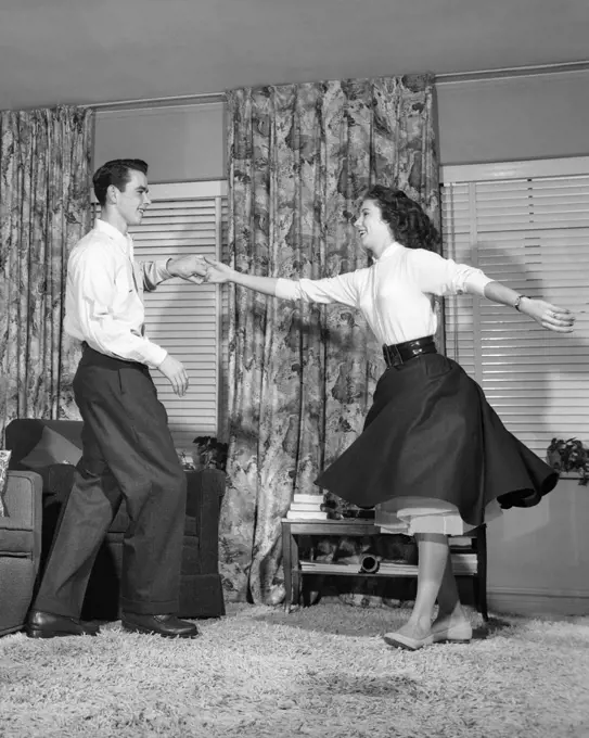 1950s TEEN BOY AND GIRL JITTERBUG DANCING TO ROCK AND ROLL MUSIC IN LIVING ROOM 