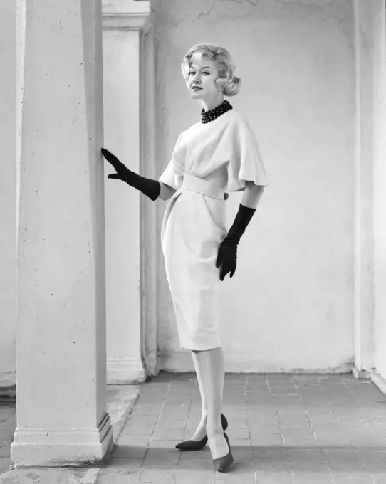 1960s FULL LENGTH PORTRAIT ELEGANT BLONDE WOMAN WEARING DRESS WITH FULL DRAPED SLEEVES LONG GLOVES POSING BY COLUMN OUTDOORS